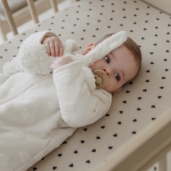 Baby met blauwe ogen ligt in een ledikant op een hoeslaken met hartjes.