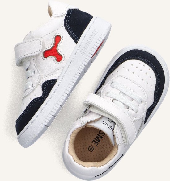 Twee witte leren sneakers met donkerblauwe accenten en rode details. Eén met X-vormig detail, andere met zichtbare zool.