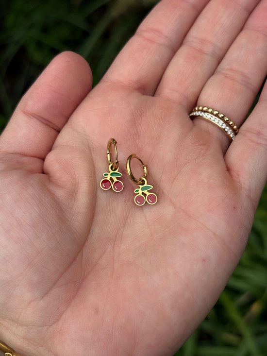 Créoles dorées avec un double breloque cerise rouge. Tenues dans une main.