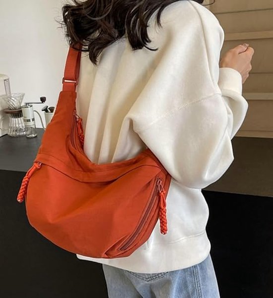 Vrouw met oranje dumpling tas, gedragen over een witte trui.
