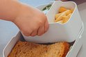 Les doigts d'un enfant attrapent un compartiment bento dans une boîte à lunch blanche.