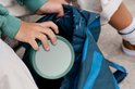 Main d'enfant plaçant un couvercle rond turquoise dans un sac à motifs bleu et noir.