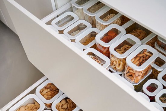 Tiroir de cuisine avec des boîtes de conservation transparentes ordonnées, remplies de divers aliments tels que des pâtes, des fruits secs et des céréales.