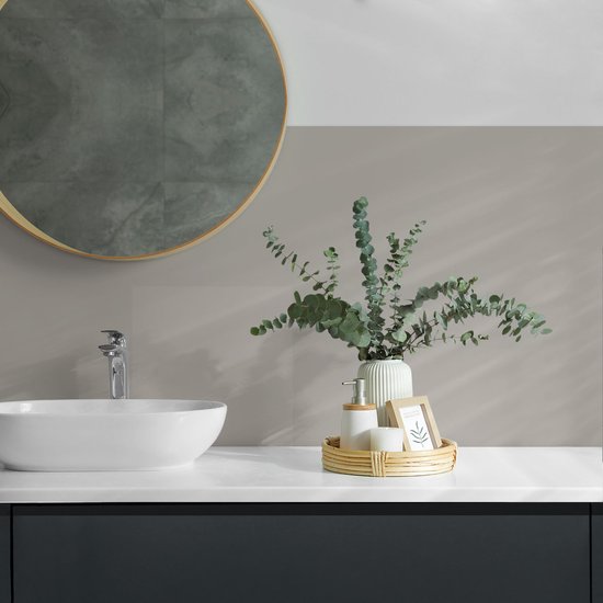 Badkamer met een witte wastafel, grijze wandtegels en een ronde spiegel met gouden rand.