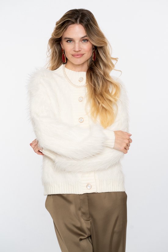 Model draagt een off-white, harig vest met knopen, gecombineerd met bruine broek en parelketting.