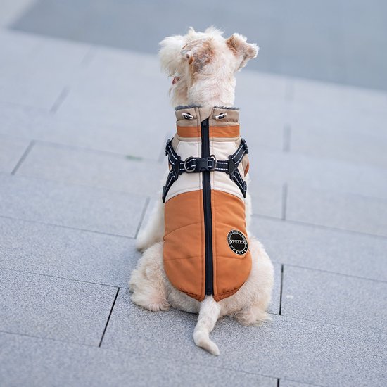 Een witte hond met een oranje-beige jasje met rits, zittend.