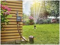 Gardena besproeiingscomputer, aangesloten op een kraan, met sproeiende sprinkler in de tuin.