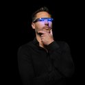 Man met zwart overhemd, denkend met een lichttherapiebril met blauw licht op.