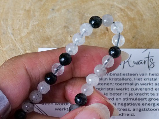 Armband met zwarte toermalijn en heldere kwartskralen, gedragen om een pols, met tekstkaart.