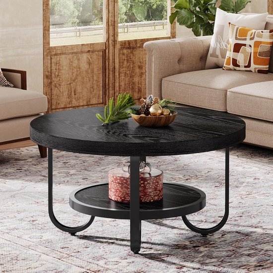 Zwarte ronde salontafel met een opbergplank, met een geschenkdoos erop. Staat bij een open haard.