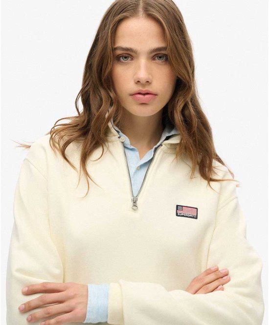 Close-up van een off-white, halve rits trui met kraag en een Amerikaanse vlag badge op de linkerborst.