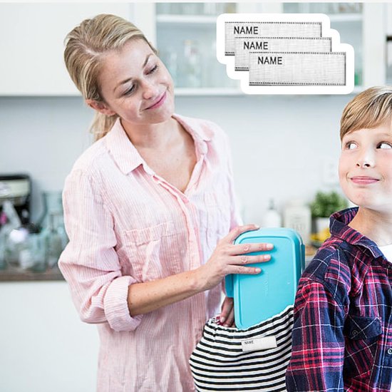 Een moeder strijkt een naamlabel op een gestreepte tas, terwijl een jongen toekijkt. Drie gestapelde naamlabels met "NAME" erop zijn zichtbaar.