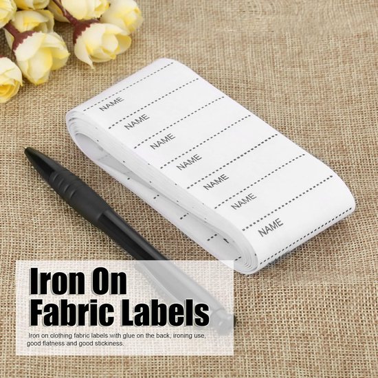 Een rol met strijkbare naamlabels met het woord "NAME" erop, met een pen. De tekst "Iron On Fabric Labels" is zichtbaar.