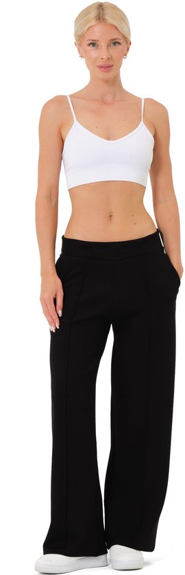 Model in zwarte wijde broek met rechte pijpen, witte top en witte sneakers.