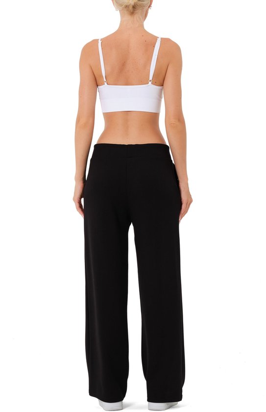 Achterzicht van model in zwarte wijde broek met rechte pijpen, witte top en witte sneakers.