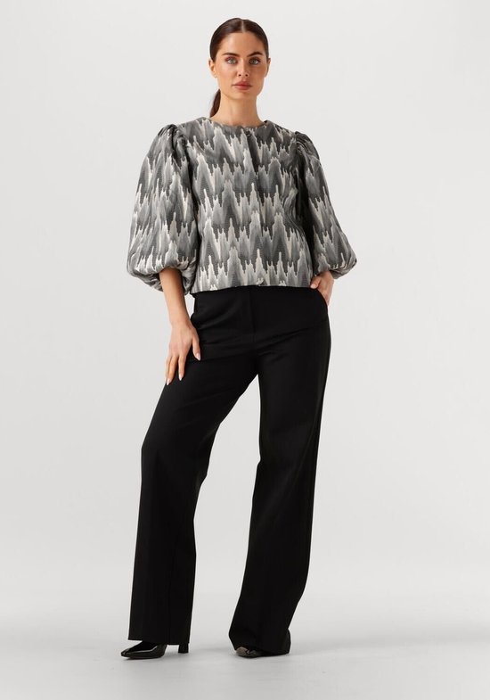 Vrouw in grijze blouse met pofmouwen en zigzag patroon, met zwarte broek.
