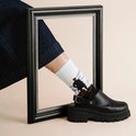 Model draagt een zwarte klomp-sneaker en een witte sok met het schilderij Wanderer boven de Nevelen van Friedrich.