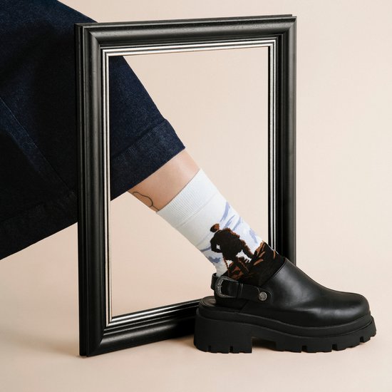 Model draagt een zwarte klomp-sneaker en een witte sok met het schilderij Wanderer boven de Nevelen van Friedrich.