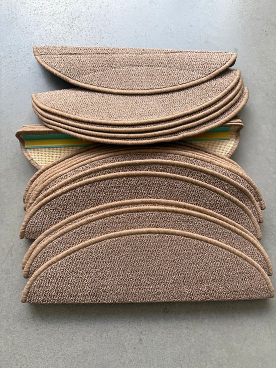 Een stapel halfronde, lichtbruine trapmatten met een gevlochten textuur en beige bies. De achterkant is van jute met een antislip laag.