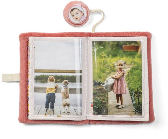 Zacht roze stoffen fotoalbum met twee foto's: kind met hond bij water en meisje met gieter. Speelgoedje met babygezichtje.