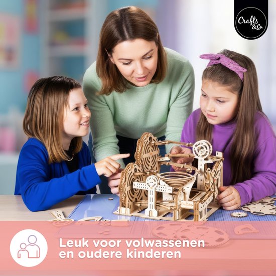 Een vrouw en twee kinderen kijken geconcentreerd naar een houten knikkerbaan.