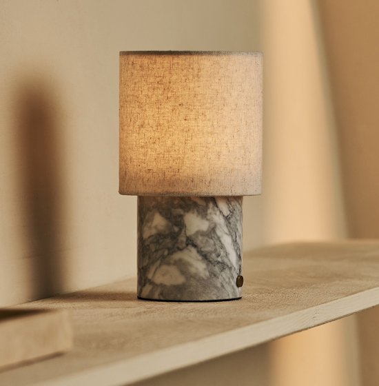 Marmeren tafellamp met beige linnen kap op een smalle houten plank.