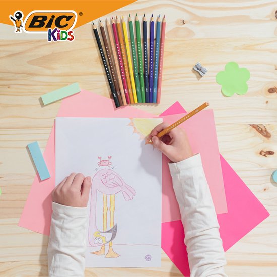 Kind tekent met een oranje Bic Kids potlood op een vel papier, omringd door gekleurde potloden en knutselspullen.