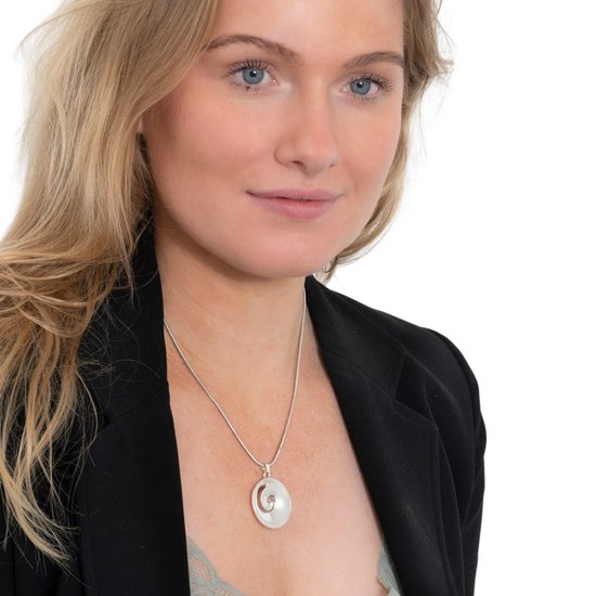 Jonge vrouw met blauwe ogen en blond haar, draagt een zilverkleurige slangenhalsketting met een ronde hanger.
