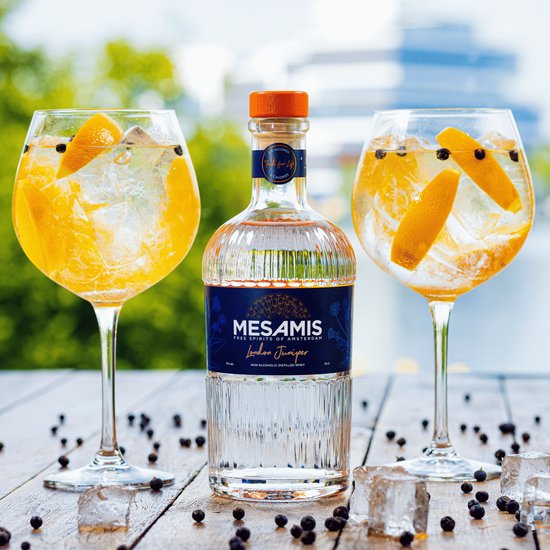 Fles Mesamis London Juniper met twee glazen gin-tonic met sinaasappelschijfjes en jeneverbessen.