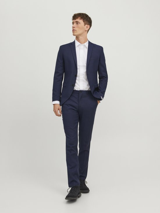 Man in donkerblauw pak met wit overhemd, loopt naar voren.