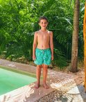 Jongen in lichtgroene zwembroek met mozaïekpatroon bij een zwembad.