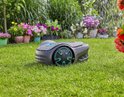 Grijze robotmaaier met turkooizen accenten op nat gras tijdens regen.