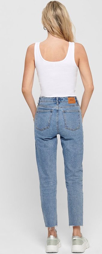 Model met een witte mouwloze top en een spijkerbroek.