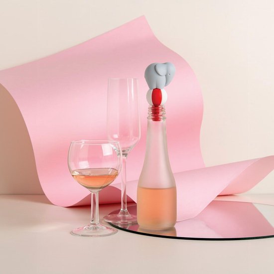 Grijze olifant wijnstopper op een fles, naast wijnglazen, met roze decoratie.