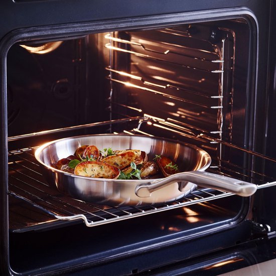 Roestvrijstalen pan met geroosterde aardappelen en kruiden in een open oven.