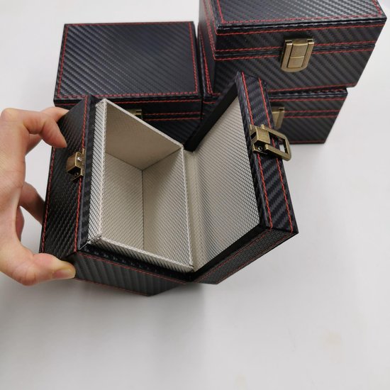 Hand opent een zwarte, carbon-look doos met rode stiksels. Meer dozen zijn op de achtergrond.