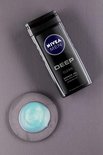 Een fles Nivea Men Deep Clean douchegel naast een ronde, grijze schijf met een klodder blauwgroene douchegel.