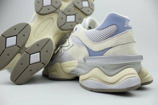 Close-up van de achterkant en zool van twee lichtgrijze New Balance 9060 sneakers met beige en lichtblauwe accenten.
