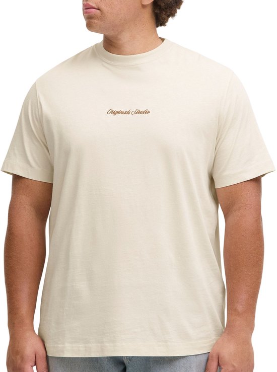 Man met krullend haar, staand, in een crèmekleurig T-shirt met 'Originals Studio' borduursel.