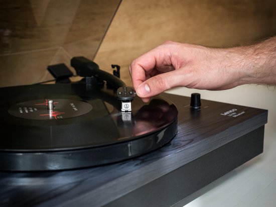 Hand plaatst naald op plaat van Lenco platenspeler.
