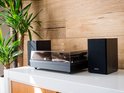 Zwarte Lenco platenspeler met twee compacte zwarte speakers op een witte kast.
