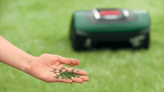 Robotmaaier met grasmaaisel op een hand, op de achtergrond.