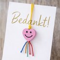 Roze hartjes bedel met lachend gezicht op een kaart met 'Bedankt!'