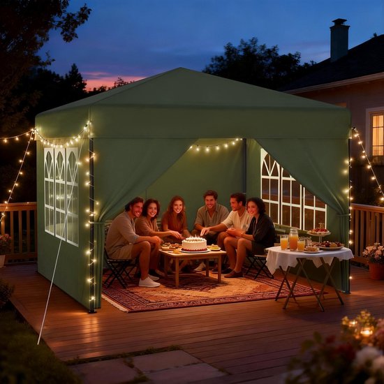 Groene partytent met puntdak en ramen, met zes mensen rond een tafel met taart op een terras.