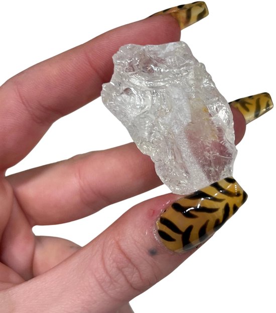 Een helder, ruw bergkristal vastgehouden tussen een duim en wijsvinger met tijgerprint nagels.