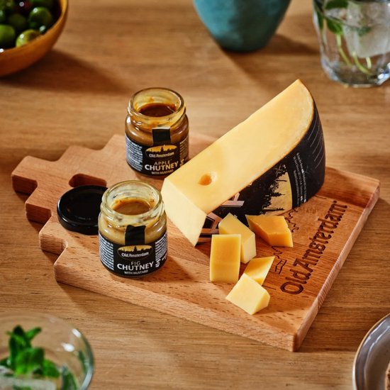 Punt Old Amsterdam kaas op een houten plank met twee potjes chutney en wat kaasblokjes.
