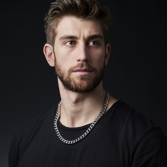 Zilverkleurige schakelketting gedragen door een man met baard en zwarte T-shirt.