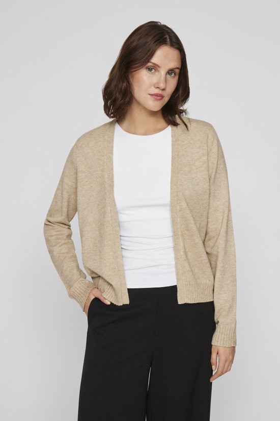 Lichtbeige gebreid vest met lange mouwen, gedragen over een wit shirt en zwarte broek.