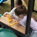Twee kinderen spelen met geel speelgoed op een houten tafel van een speeltoestel.