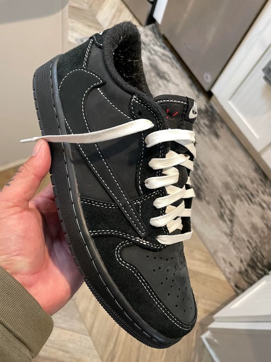 Zwarte Nike Air Jordan 1 lage sneaker met witte veters, vastgehouden in een hand.